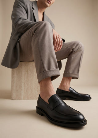 Man wearing black leather loafers styled with relaxed tailored trousers.