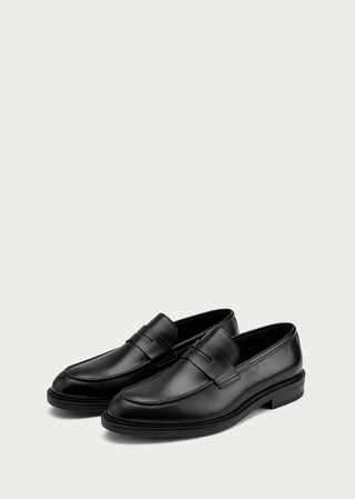 Pair of black leather loafers on a light neutral background.