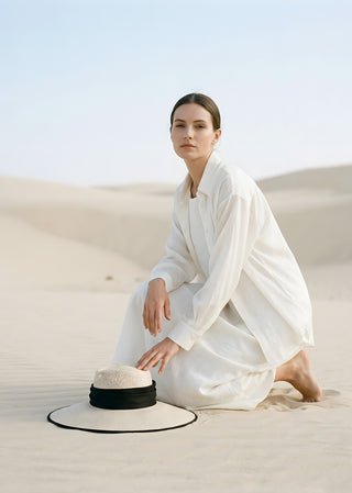 Woman in white clothing seated in a desert landscape beside the handcrafted Copardo Lucia Hat