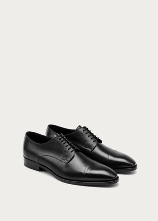 Pair of black leather lace-up shoes with elegant minimalist silhouette on a light neutral background.