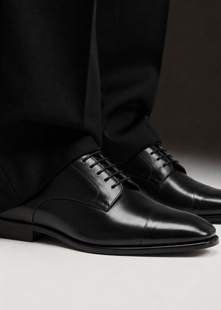 Man wearing black leather lace-up shoes styled with tailored black trousers.
