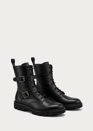 Pair of black leather buckle boots with rugged sole on a light neutral background.